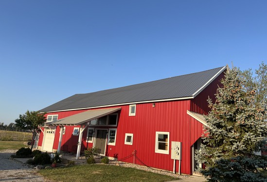 Side view of a red barn with a freshly installed metal roof and white trim